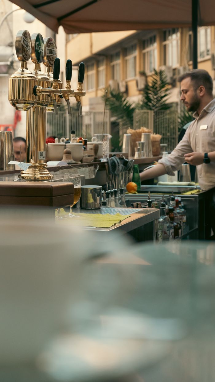 Bustling outdoor bar with a bartender preparing drinks in a city setting.